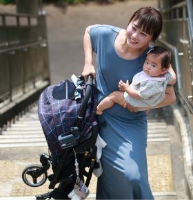 a woman carrying on a child in one hand and a pram in the other hand, climbing the stairs