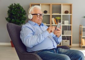 Stariji čovek koristsi telefon i slušalice sa osmehom na licu pozitivan primer