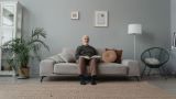 blind man is sitting on a couch and reads a book in braille