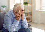 an elderly man sits alone and covers his face with his hands
